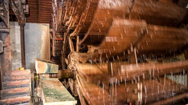 Ein großes altes Schaufelrad aus Holz, über das Wasser läuft.