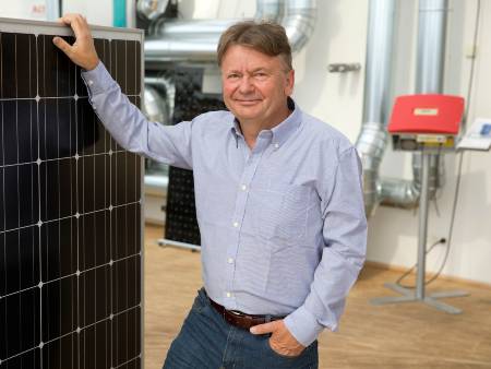 Ein Mann in hellblauem Hemd und Jeans steht neben einem PV-Modul.