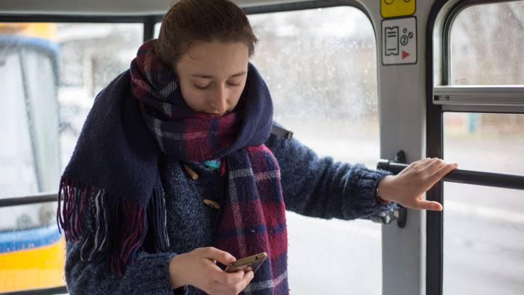 Dieselbe junge Frau wie oben, steht in der Straßenbahn und schaut auf ihr Handy.