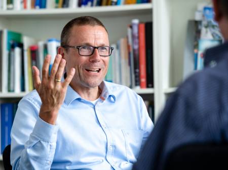 Ein Mann mit Brille und aufgeknöpftem Hemd hebt im Gespräch gestikulierend die rechte Hand.