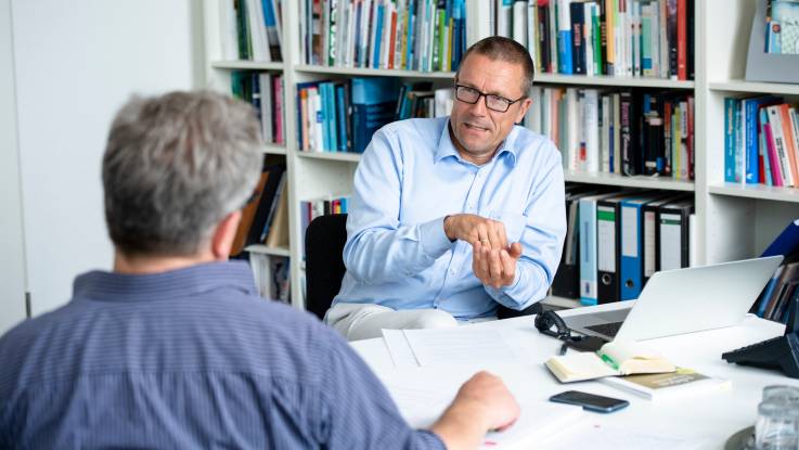 Ein Interviewer, ihm gegenüber ein Mann vor einer Bücherwand, der gestikulierend die Hände hebt