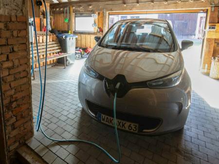 In einer Garage steht ein silberner Kleinwagen, der mit einem Ladekabel verbunden ist.