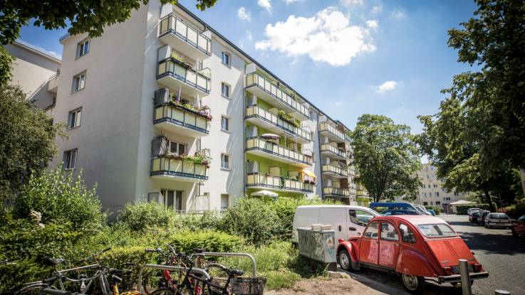 Eine 1960er-Jahre Wohnanlage, auf dem Parkplatz steht eine rote 2CV.