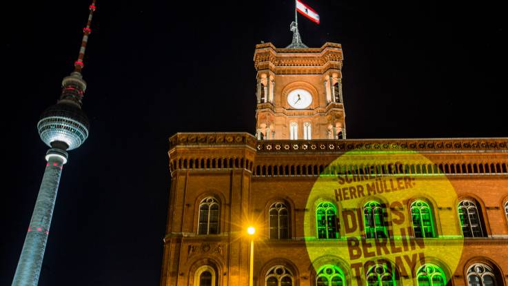 Das Rote Rathaus und der Berliner Fernsehturm im Bild. Auf das Rathaus ist ein großer Kreis mit dem Slogan «Herr Müller Divest Berlin today» projiziert.