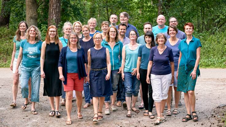 Sommerliches Gruppenfoto im Wald: Eine etwa 20-köpfige Gruppe, bestehend zu etwa dreiviertel aus Frauen und einem Viertel Männer.