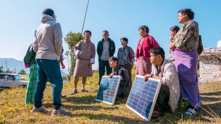 Eine Gruppe von Menschen steht locker gruppiert auf einer Wiese und zeigen zwei PV-Module.