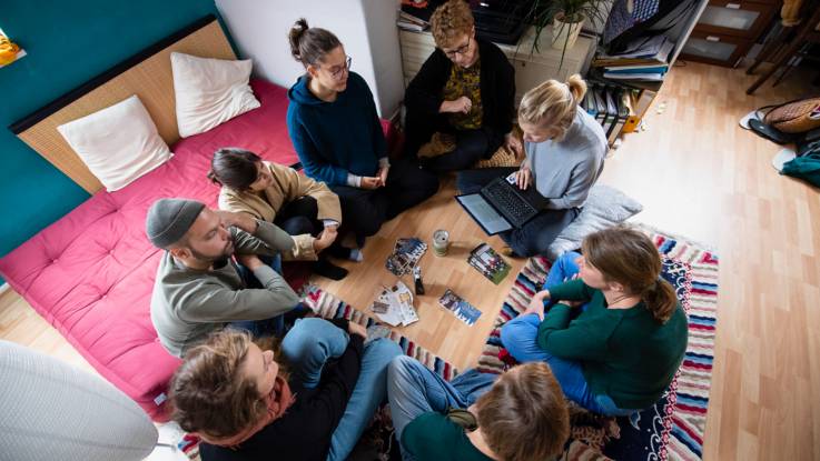 Acht junge Menschen bilden, von oben fotografiert, einen Sitzkreis.