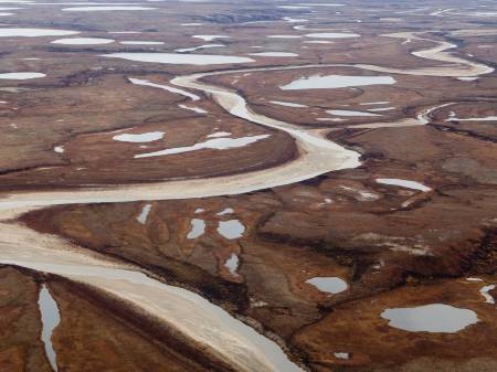 Luftbild einer rostbraunen, kargen Landschaft mit vielen kleinen Wasserflächen und einem Fluss.