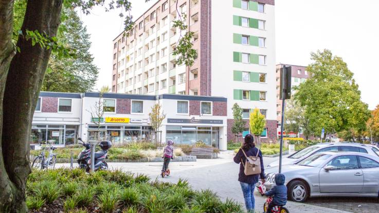 Eine zweigeschossiger Gebäuderiegel an einem Platz, dahinter ein achtgeschossiger Wohnblock