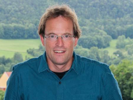 Portrait eines jungen Mannes mit Brille vor grüner Kulisse.