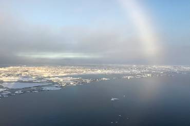 Blick aufs Meer, im Hintergrund ein Regenbogen. Auf dem Meer viele kleine Eisschollen.