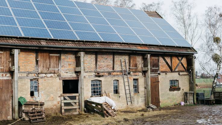 Ein altes Stallgebäude bei grauem Winterwetter, darauf PV-Module