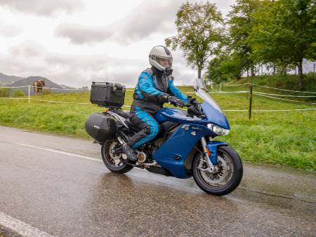 Auf einer Landstraße fährt ein E-Motorrad im Regen an einer Pferdeweide vorbei.