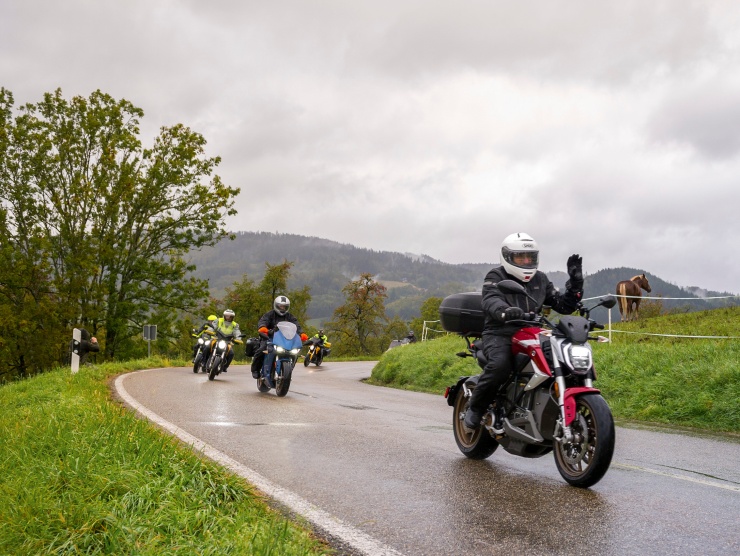 Eine Gruppe von Motorrädern im Regen, im Vordergrund hebt ein Mann den Daumen.