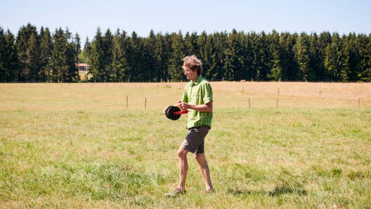 Auf einer vertrockneten Wiese rollt ein Mann Draht für einen Elektrozaun aus.