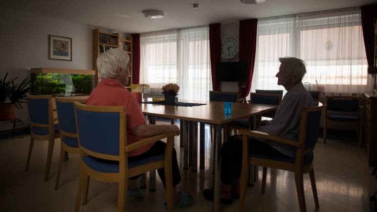 Zwei Damen sitzen in einem abgedunkelten Zimmer an einem Tisch