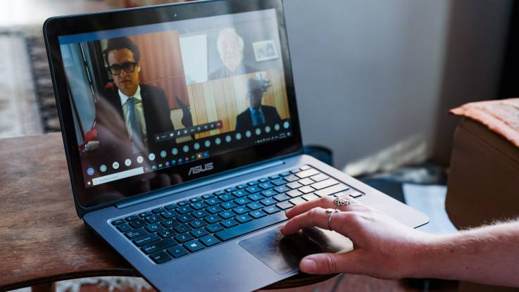 Der Blick auf den Laptopbildschirm der jungen Frau zeigt eine Konferenzsituation mit drei älteren Männern.