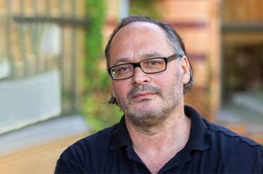 Kopfportrait eines Mannes mit Halbglatze und Brille im Sommer in einem Hinterhof.