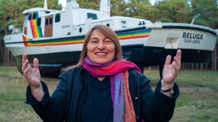 Eine Frau vor einem regenbogenfarben bemalten Boot, das auf einer Wiese steht