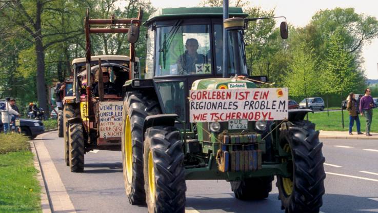 Eine Reihe von Treckern auf einer sommerlichen Landstraße. Auf dem Trecker vorne ein Schild mit der Aufschrift: "Gorleben ist ein regionales Problem .. wie Tschernobyl."