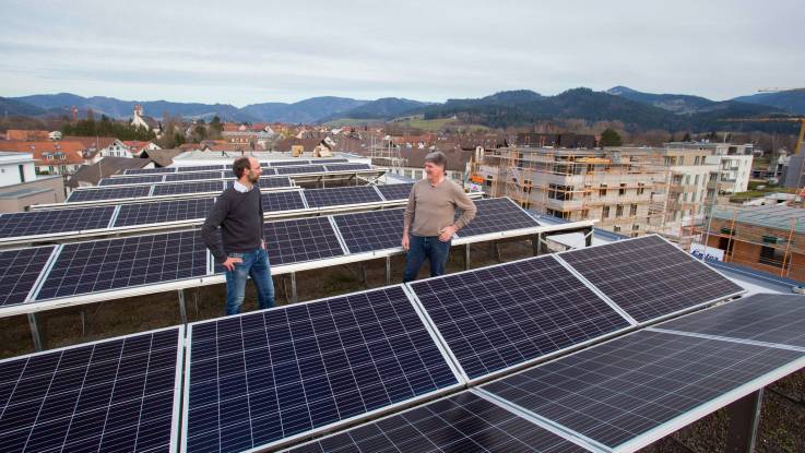 Zwei Herren stehen auf einem Flachdach, das mit Solarpanelen bestückt ist, im Hintergrund der Schwarzwald.