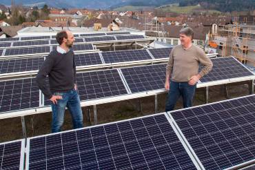 Zwei Männer stehen zwischen PV-Modulen auf dem Dach eines Gebäudes.