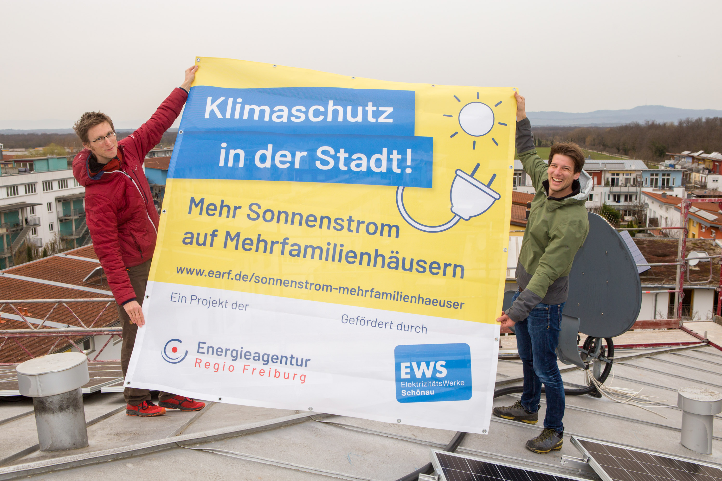 Zwei Männer halten ein Plakat des Projektes hoch. 