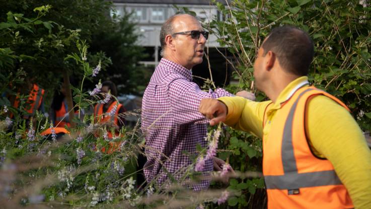 Two middle-aged men stand in the middle of the garden and greet each other with an elbow salute.