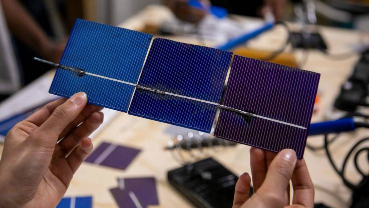 Two female hands hold three small solar panels connected with soldering wire.