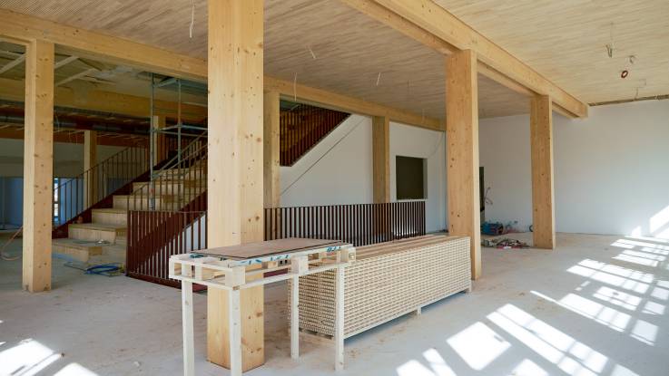 Ein von wuchtigen Holzträgern geprägter Raum, im Hintergrund ist eine Treppe zu erkennen.