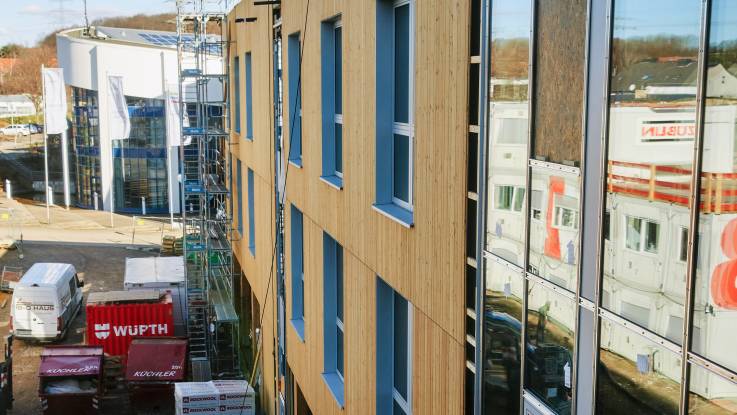 Blick auf eine fast schon fertiggestellte, mit Holz verkleidete und von zahlreichen Fensterflächen durchbrochene Fassade