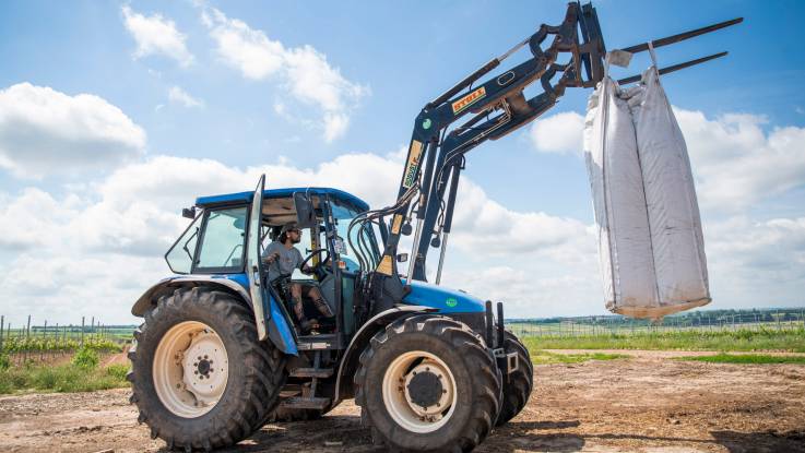 Im Weinberg transportiert ein Traktor einen großen weißen Sack.