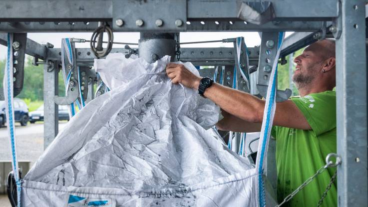 In einer Anlage hält ein Mann einen großen weißen Plastiksack unter ein Rohr, durch das die Pflanzenkohle in den Sack gelangt.