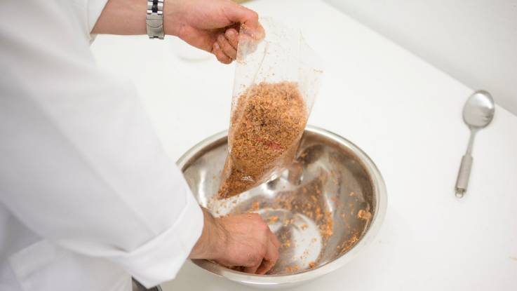 Ein Mann im weißen Kittel füllt Material, dass aussieht wie Holzspäne, in eine kleine Plastiktüte.