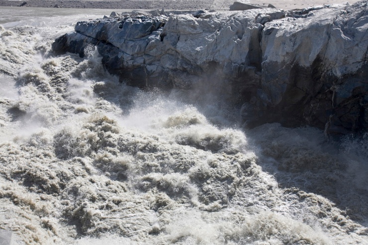 An einem Eisfelsen rauschen riesige Wassermassen entlang.