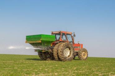 Ein Trecker bringt auf einem Acker weißen pulverförmigen Dünger aus.