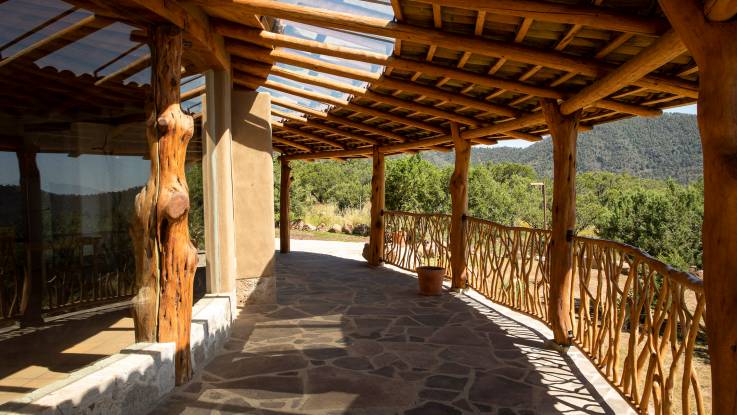 Eine fast kreisförmig um das Haus laufende überdachte offene Veranda ist aus organisch gewachsenem Holz gebaut.