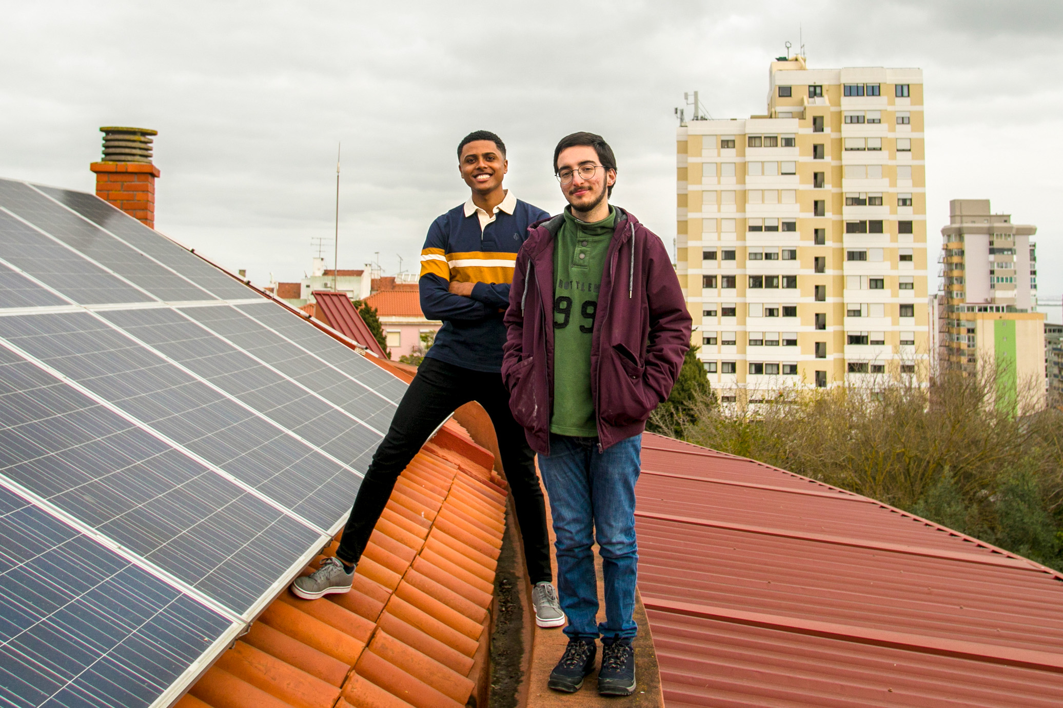 Inmitten einer Dachlandschaft mit PV-Anlagen stehen zwei junge Männer.