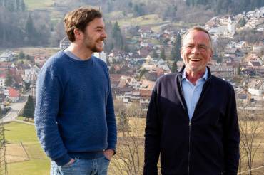 Drescher und Sladek stehen sich lachend gegenüber, im Hintergrund der Ort Schönau.