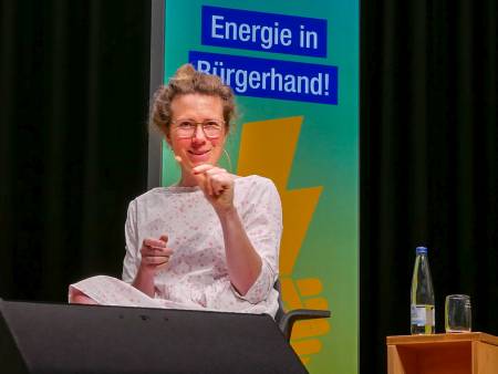 Eine junge Frau spricht auf dem Stromseminar auf dem Podium, ein Mann hört aufmerksam zu.