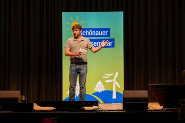 Sebastian Sladek spricht auf der Bühne mit ausladender Geste.