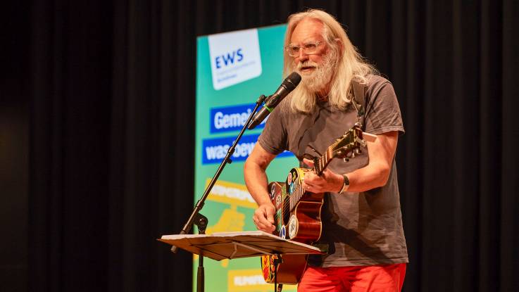 Ein älterer Mann mit langen grauen Haar und Bart singt und spielt Akustikgitarre.