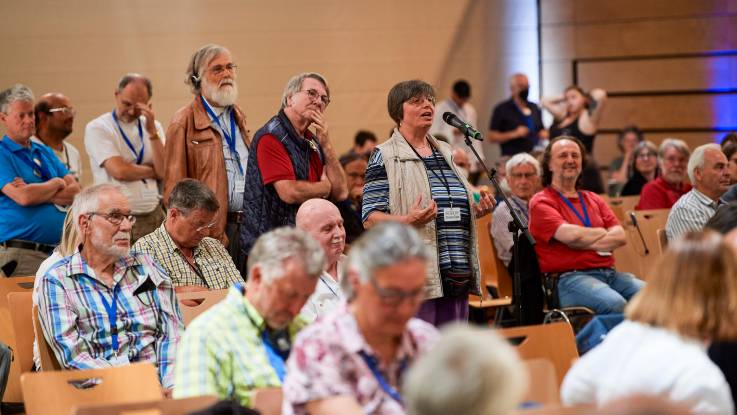 Vor dem Mikrofon im Saal stehen mehrere Zuschauer Schlange, sitzende Zuschauer hören zu.