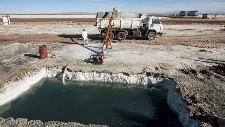 Ein Arbeiter steht in einer braun-weißen flachen Landschaft neben einem eckig ausgeschachteten Becken, aus dem Sole in einen LKW gepumpt wird.