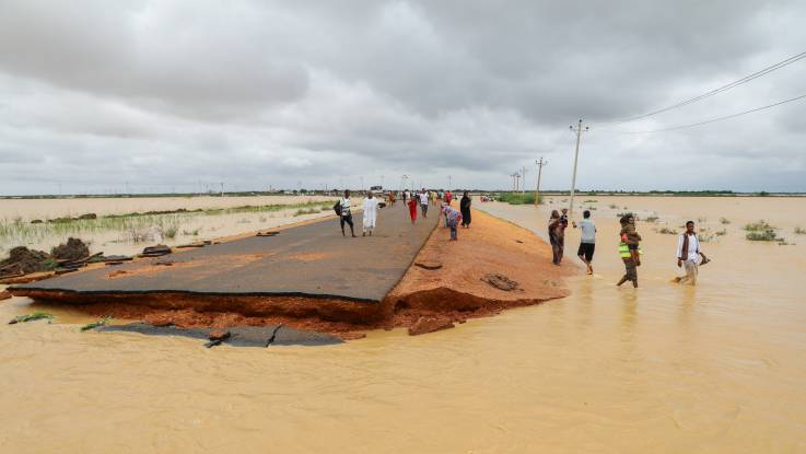 Menschen stehen auf und neben einer erhöhten Straße, die abrupt endet, weil sie vom Hochwasser weggespült wurde.