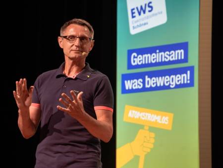 Vor einer grün-gelben Stele mit dem Slogan "Gemeinsam was bewegen" spricht ein Martin Halm zum Publikum.