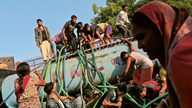 Auf und vor einem Wassertank stehen zahlreiche Menschen – grüne und blaue Schläuche befördern Wasser aus dem Tank.