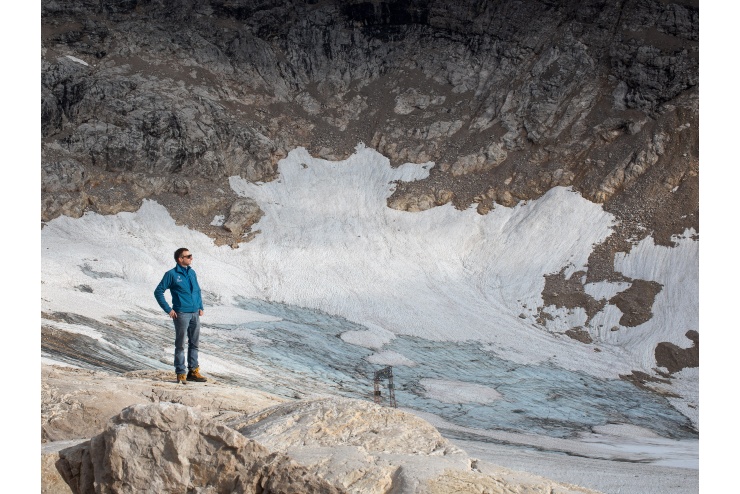   Ein Mann in blauer Jacke steht in einem Talkessel und blickt in die Ferne – unter dem Schnee kommt Geröll zum Vorschein.