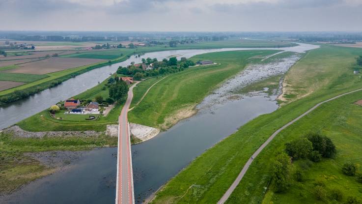 Über einen renaturierten Flussarm hinweg spannt sich eine Brück zu einer kleinen Gemeinde in Insellage.