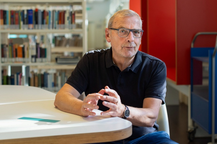 Sighard Neckel sitzt am Tisch in einer Bibliothek und hält die Hände zu einem Gefäß geformt.